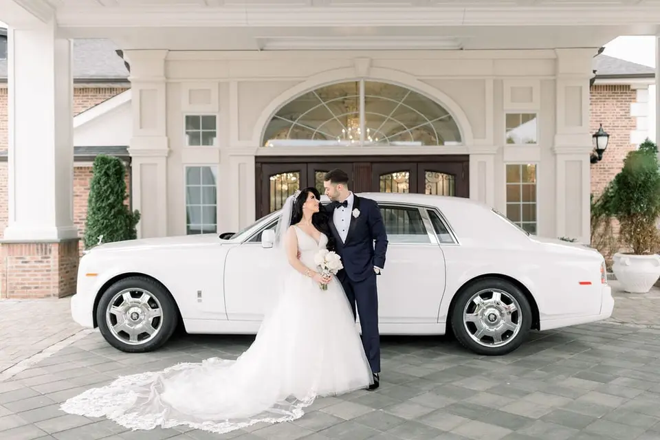 The bride and groom kiss beside a white Rolls-Royce outside The Rockleigh.