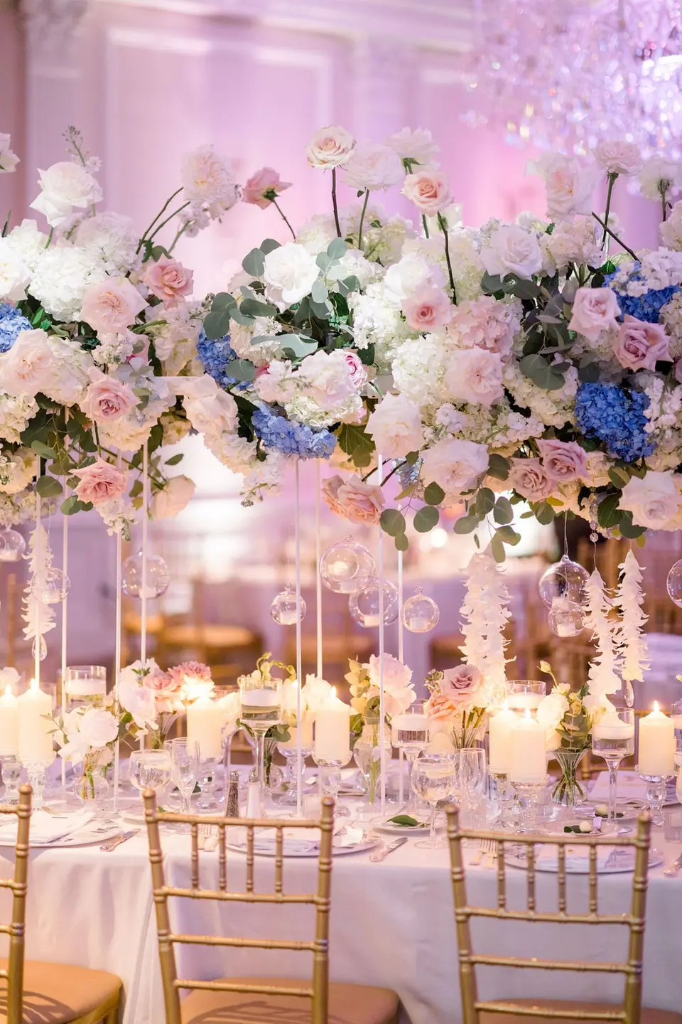 A tall arrangement of white roses and blue hydrangeas above glass orbs and candles.