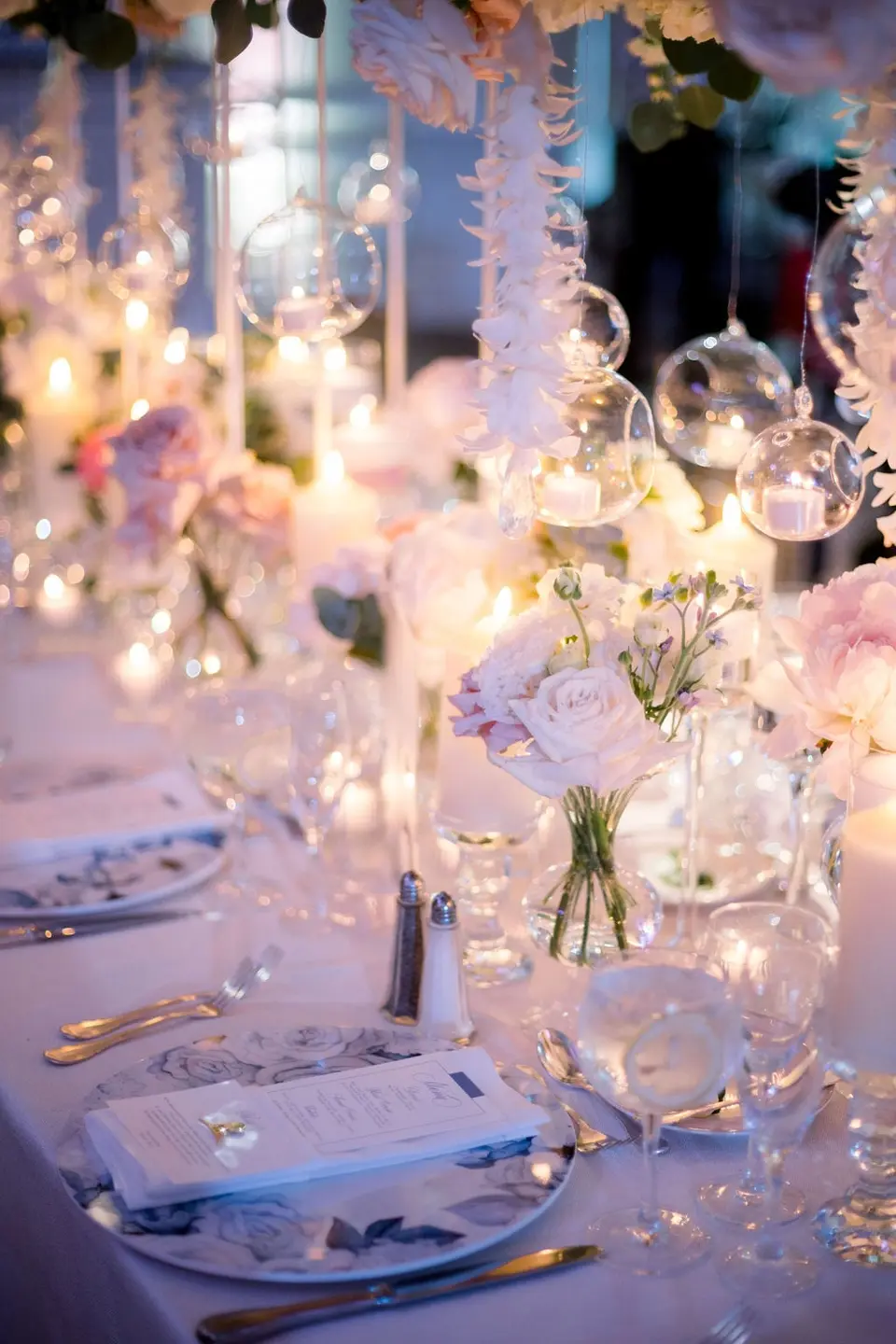Candles, glass orbs and white roses along a long table, menus set on blue floral chargers.
