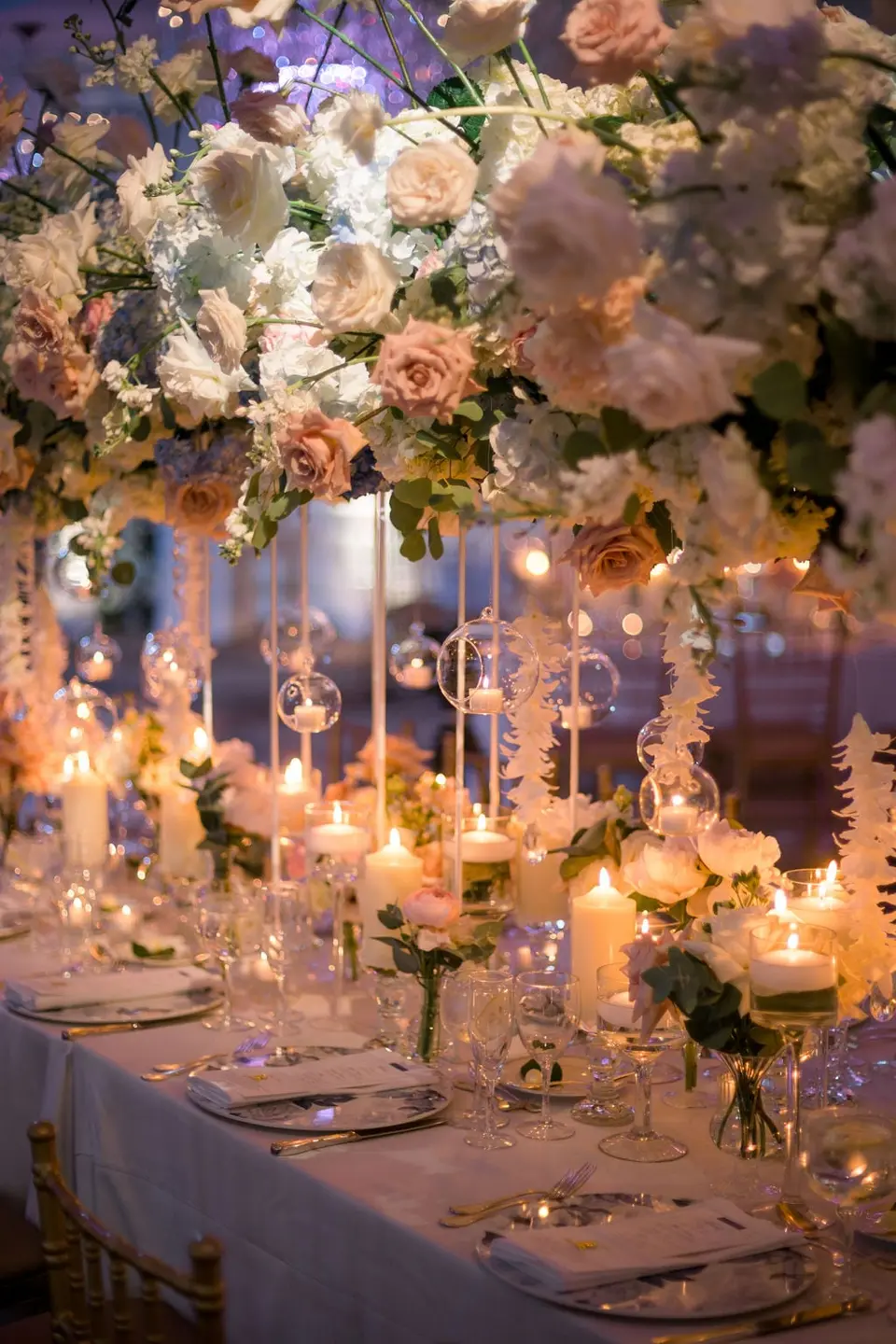 Pink roses and hanging white flowers above a candlelit table.