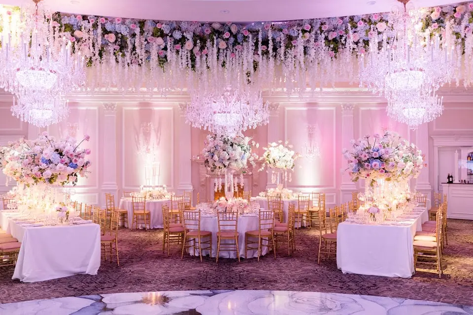 The ballroom beneath hanging white flowers and crystal chandeliers, tables set with pastel arrangements.