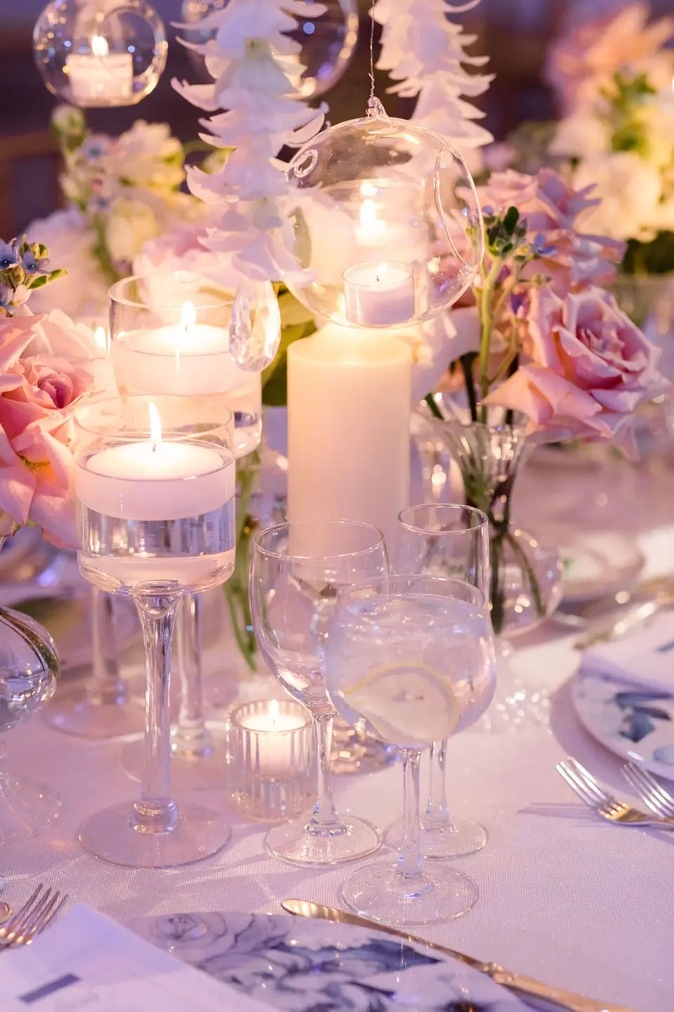 Floating candles, pillar candles and pink roses among the glasses on the table.