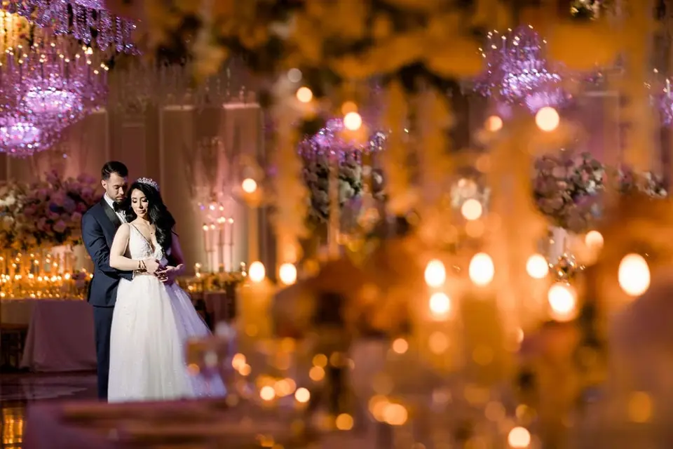 The groom holds the bride from behind, candles glowing out of focus in front of them.