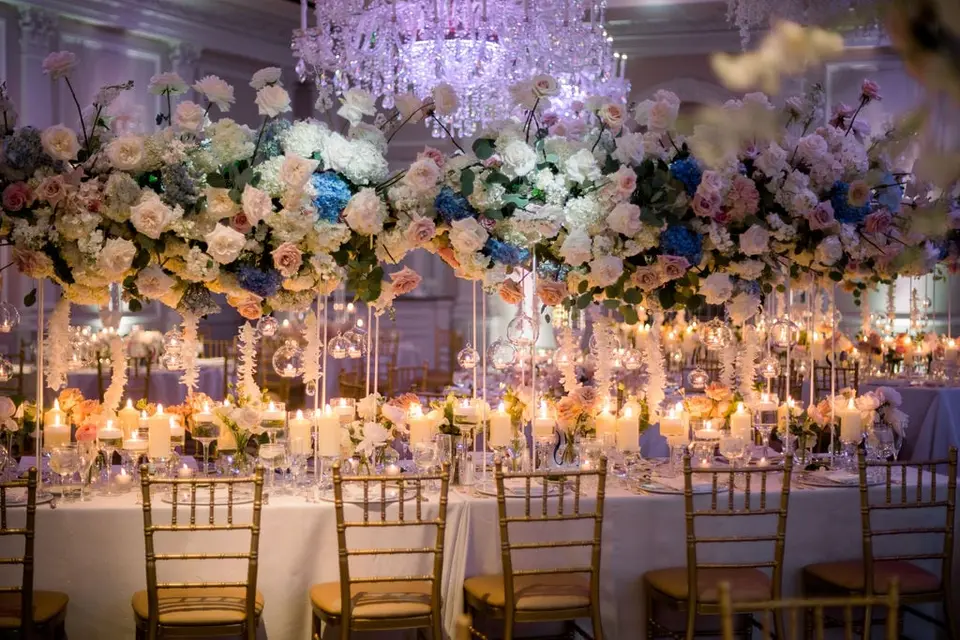 Tall arrangements of white, blush and blue flowers above candlelit tables beneath a crystal chandelier.