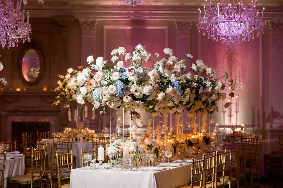 Tall flower arrangements along a candlelit table, a gilt mirror and chandeliers on the pink-lit walls.
