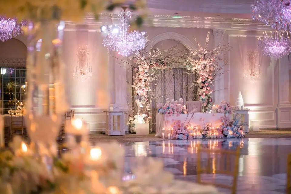 The sweetheart table beneath a flowered arch, seen across the empty dance floor.
