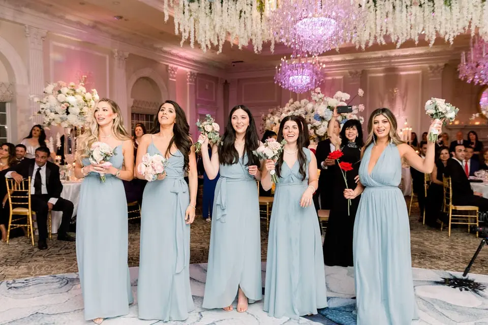 The bridesmaids in pale blue enter the ballroom, bouquets raised.