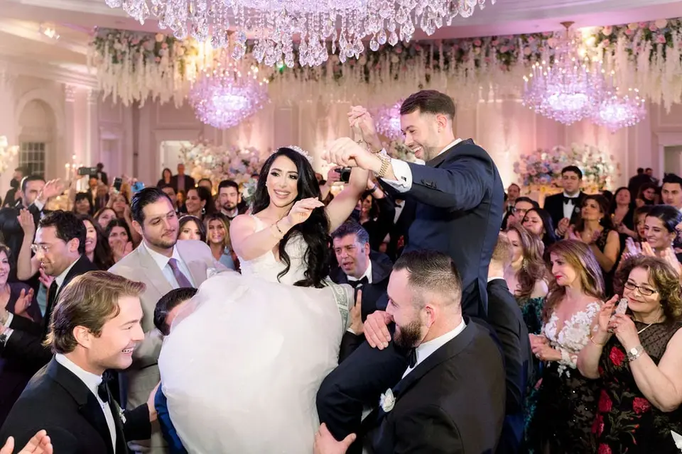 Guests lift the bride and groom on chairs above the crowd.