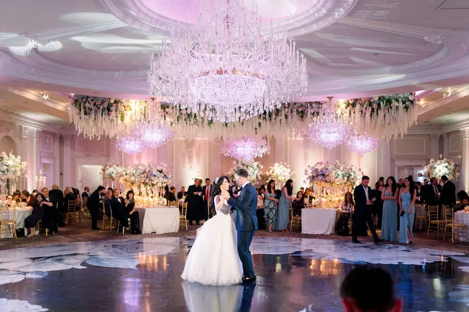 The first dance on a floor painted with white flowers, guests watching from the tables.