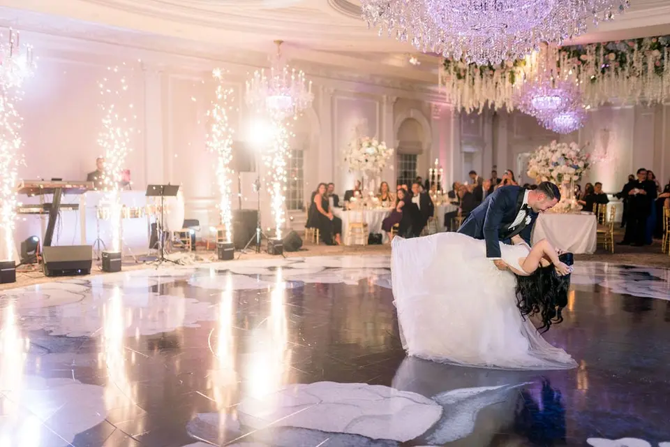 The groom dips the bride on the dance floor as sparklers go up behind them.