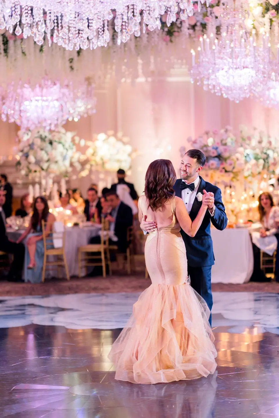 The groom dances with a woman in a peach mermaid gown as guests watch.