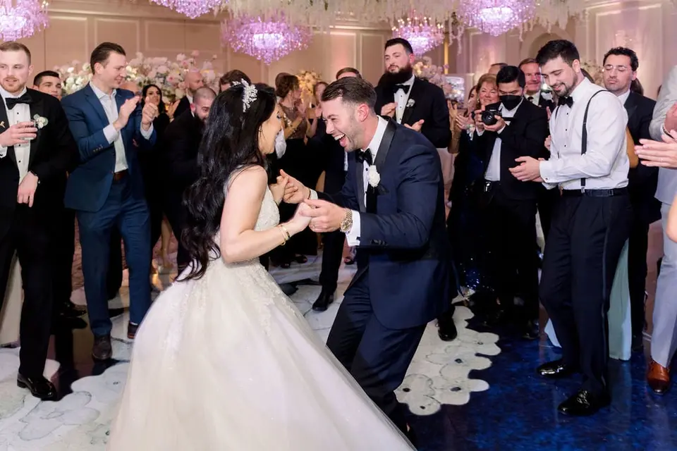 The bride and groom dance face to face in a circle of cheering groomsmen.
