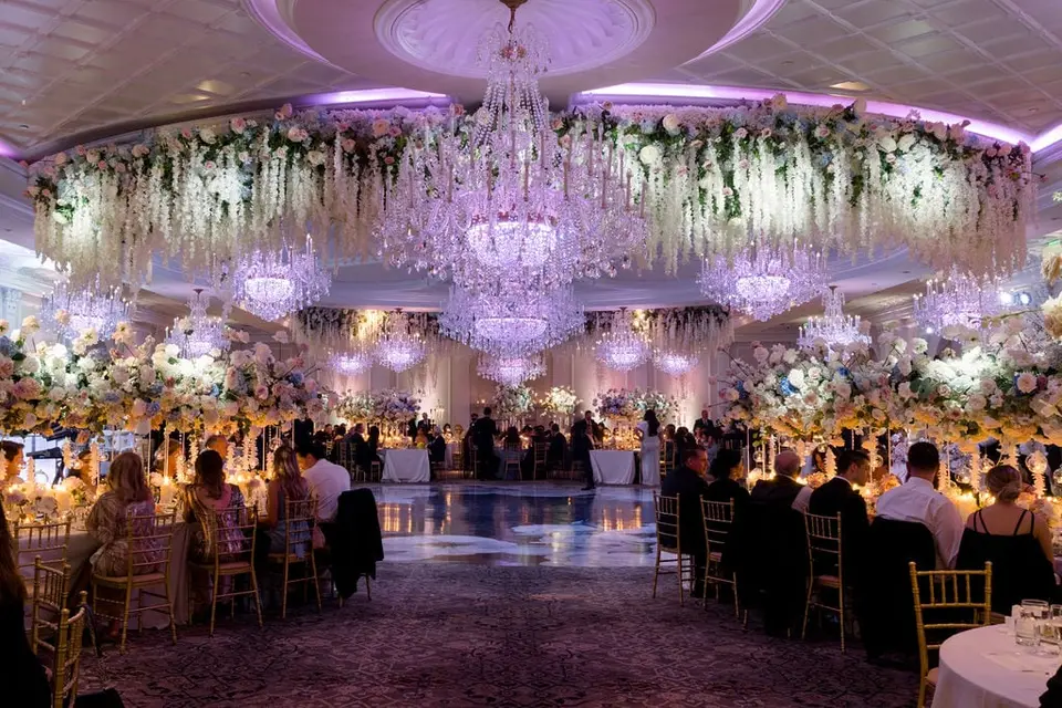 A wide view of the ballroom from the dance floor, chandeliers and hanging flowers over every table.