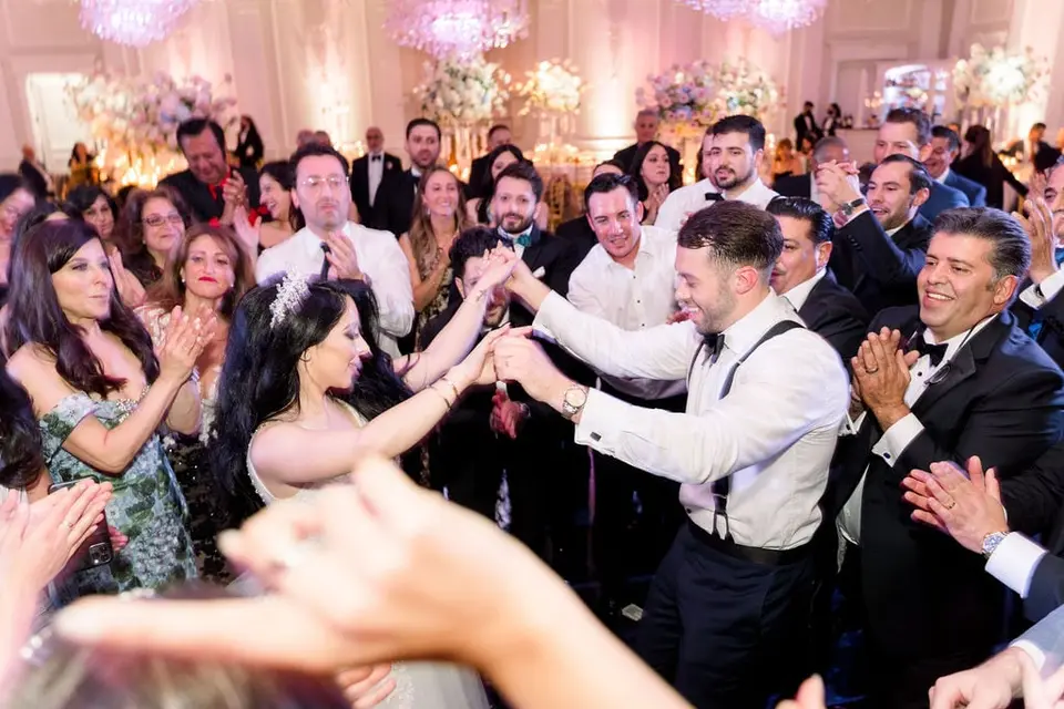 The bride and groom dance hand in hand as guests clap around them.