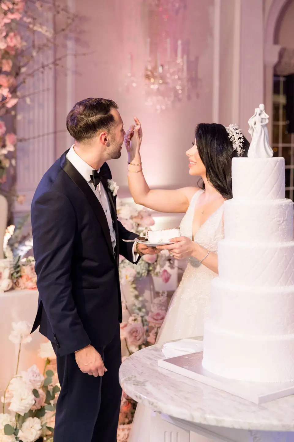 The bride dabs cake on the groom's nose as he laughs.