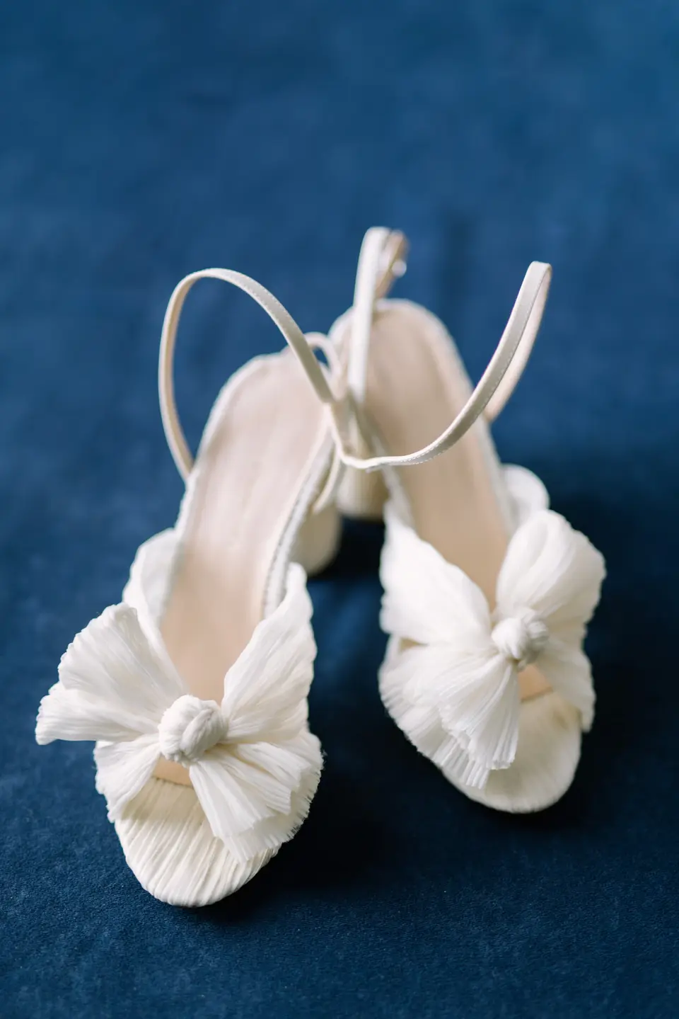 White bridal sandals with knotted bows, set on deep blue velvet.