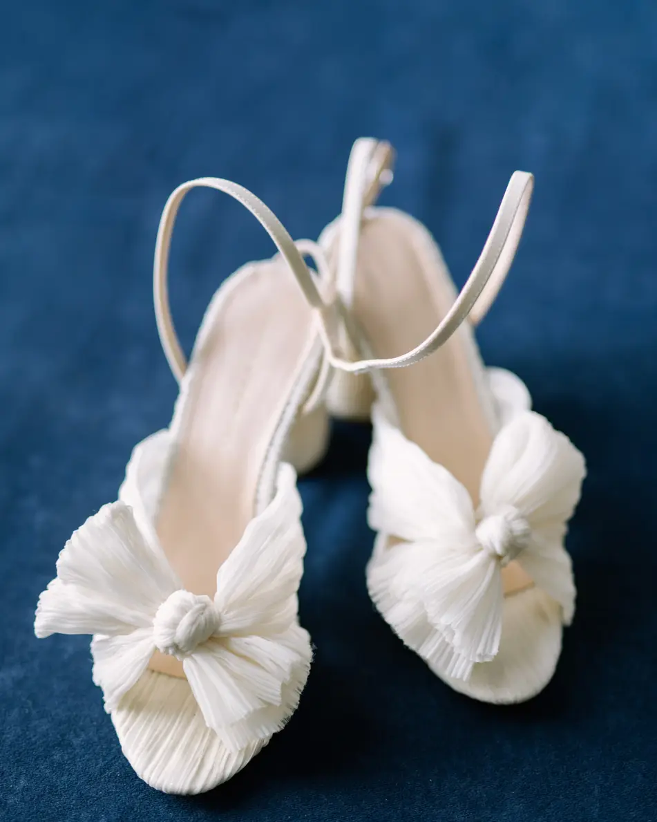 White bridal sandals with knotted bows, set on deep blue velvet.