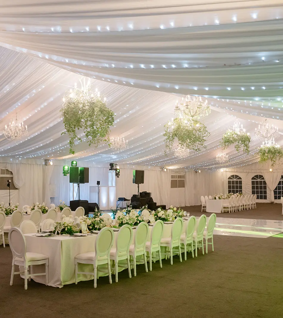 The tent on the lawn, set for dinner beneath a draped white ceiling and chandeliers hung with greenery.