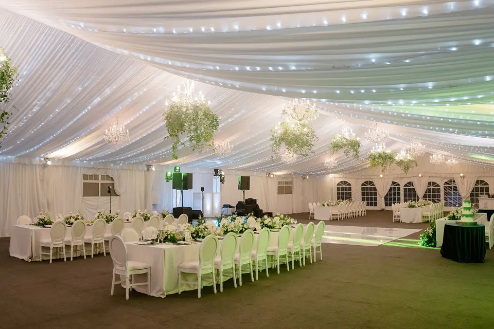 The tent on the lawn, set for dinner beneath a draped white ceiling and chandeliers hung with greenery.