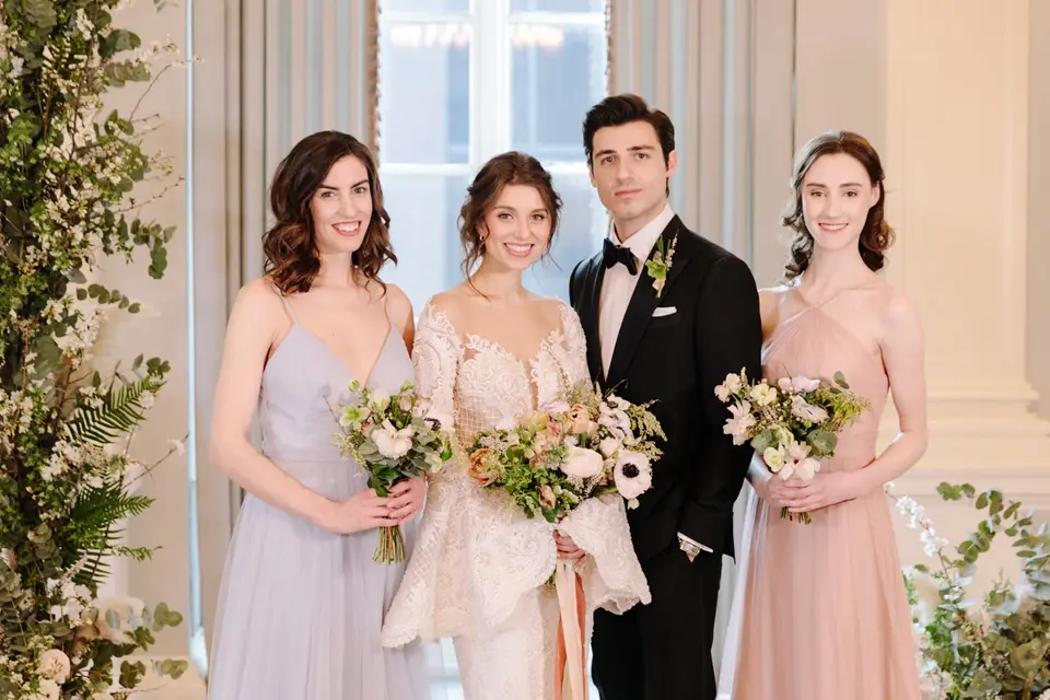 The couple with two bridesmaids in lavender and blush, holding loose bouquets, in the ballroom.