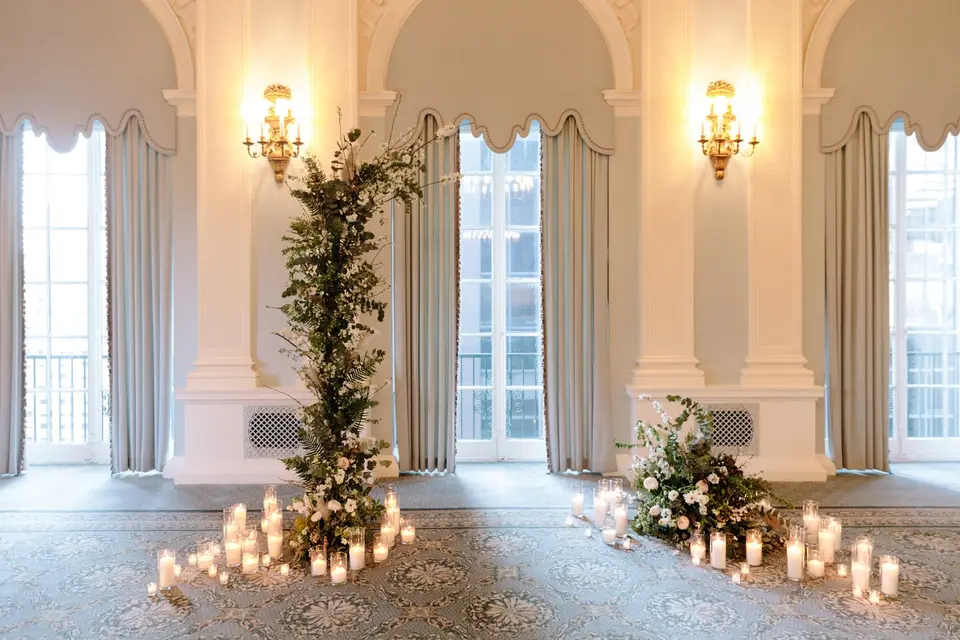 The ceremony space: a column of greenery and white flowers before tall windows, candles on the floor around it.