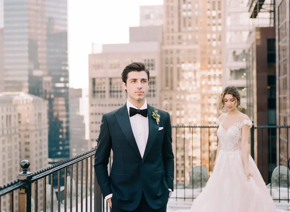 On the roof terrace, the groom waits as the bride walks toward him for the first look, Midtown behind.