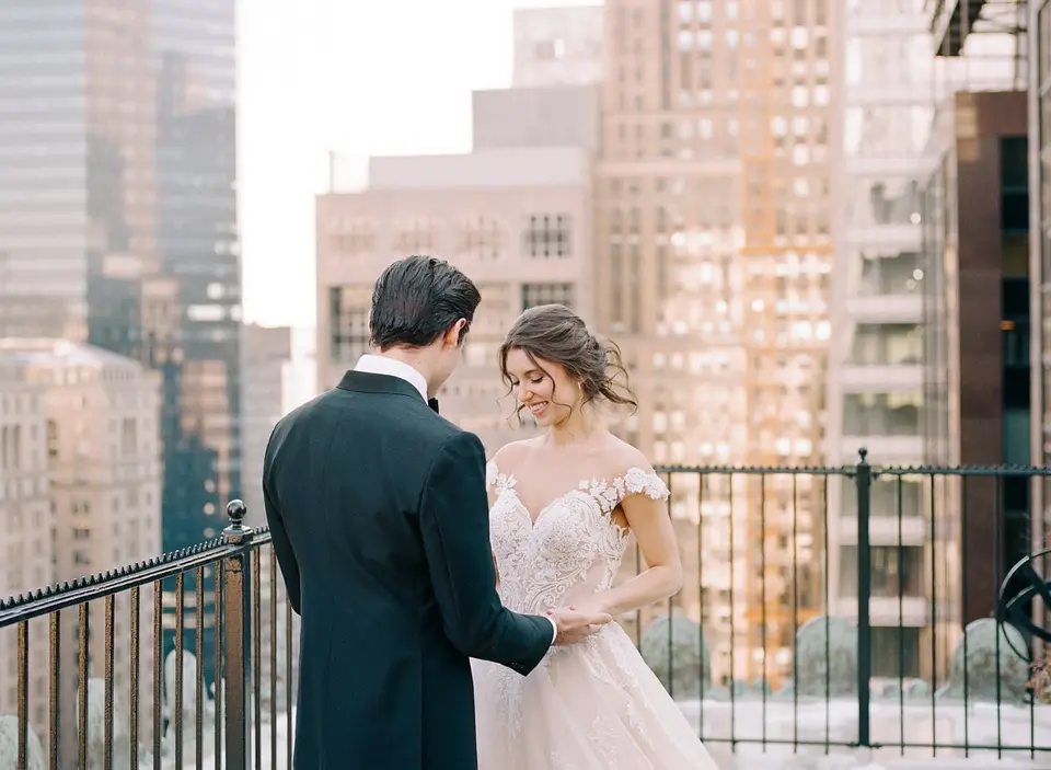 The groom and bride face each other on the terrace, her eyes lowered to his hands.