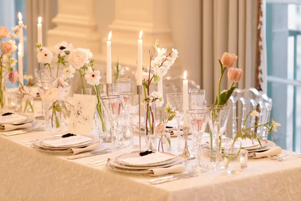 A long table with taper candles, single stems of tulips and anemones in bud vases, and cut-glass goblets.