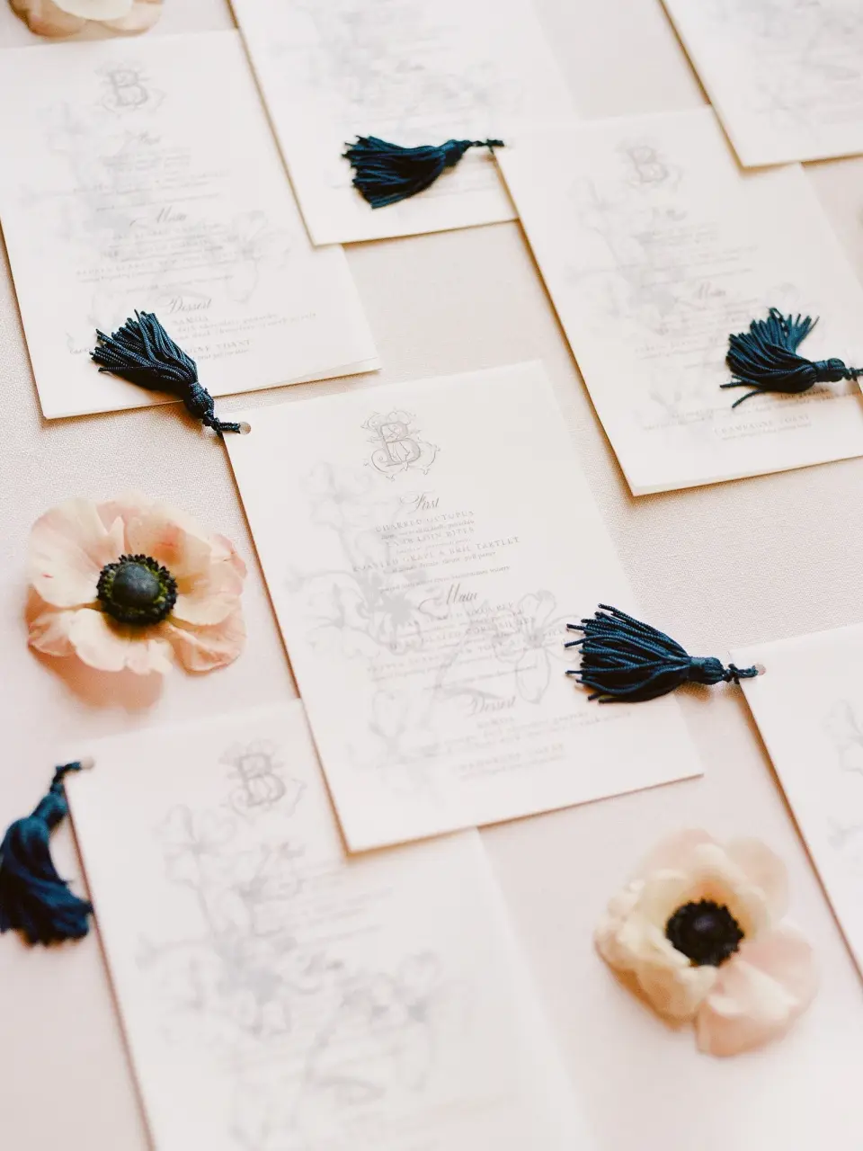 Menu cards with blue tassels among anemone blossoms.