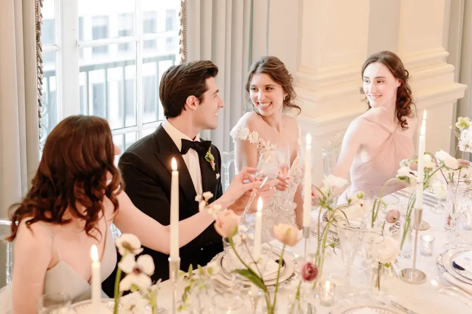 The couple and their friends laugh together at the candlelit table.