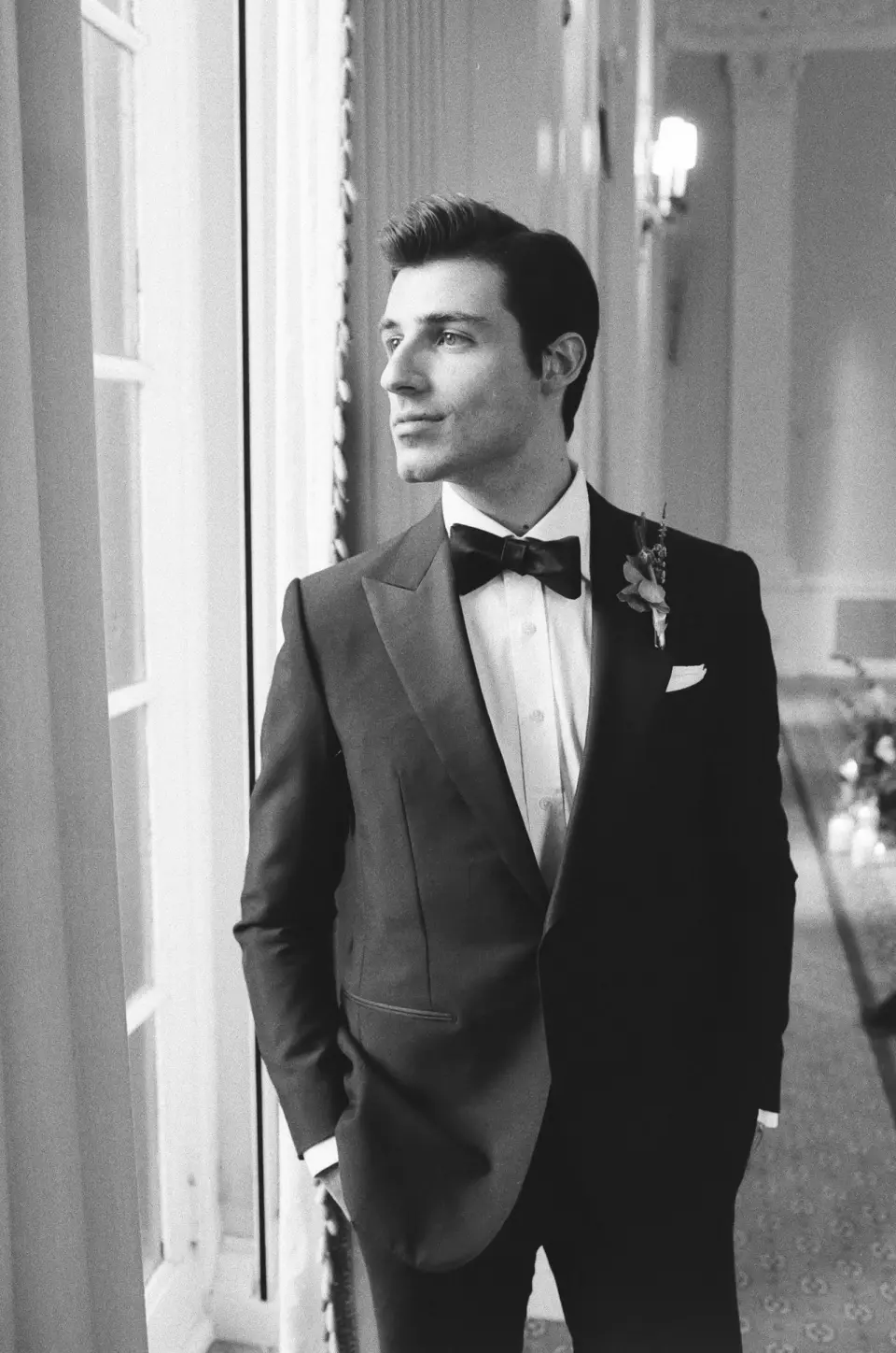 The groom looks out of a tall window. Black and white.