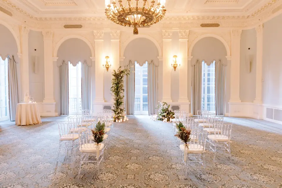 The ballroom set for the ceremony, clear chairs either side of the aisle and a column of flowers at the front.