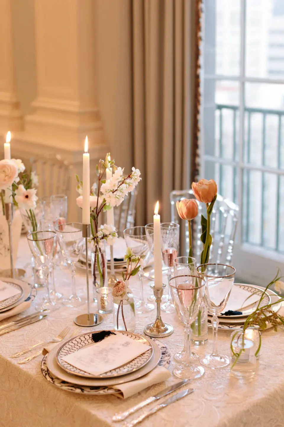 A place setting at the long table, candles, tulips and blossom in glass vases around it.