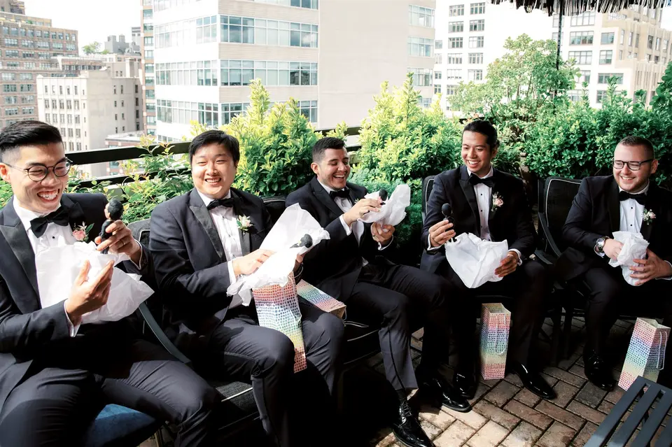 The groomsmen laugh as they open gifts on a rooftop terrace.