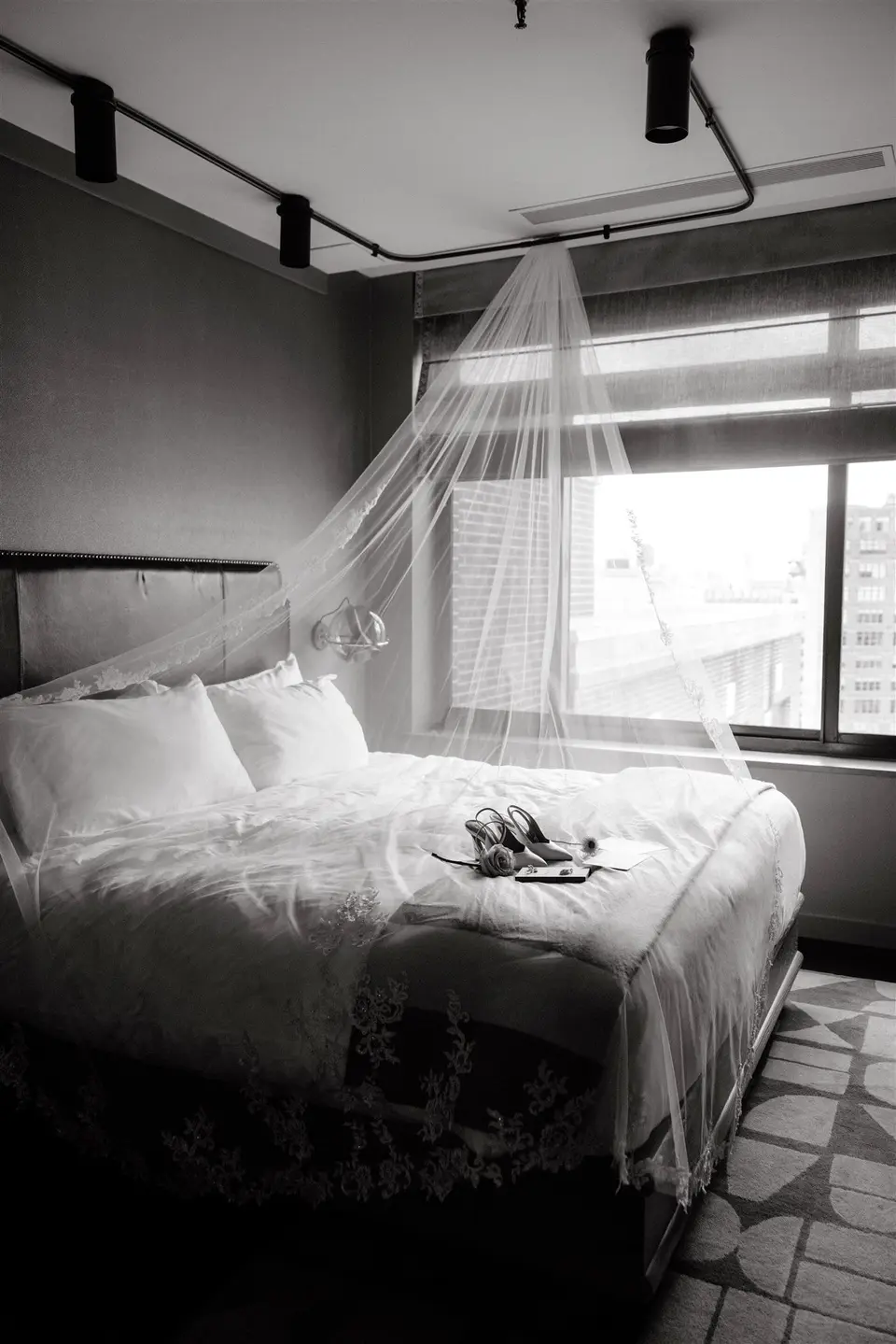 The veil hanging above the bed in a hotel room, the bride's shoes on the covers. Black and white.