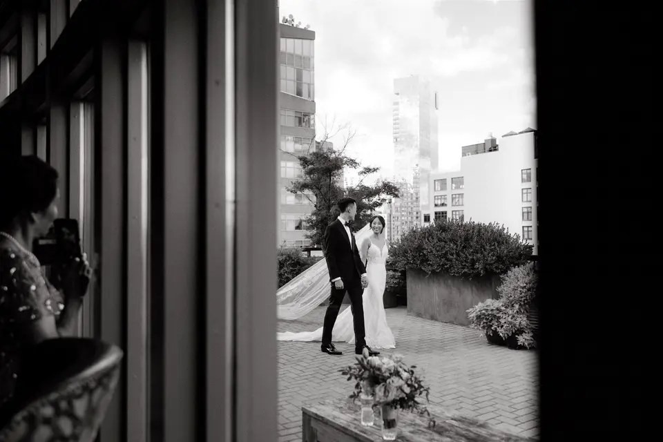 Seen through a doorway, the groom turns to see the bride on the terrace. Black and white.