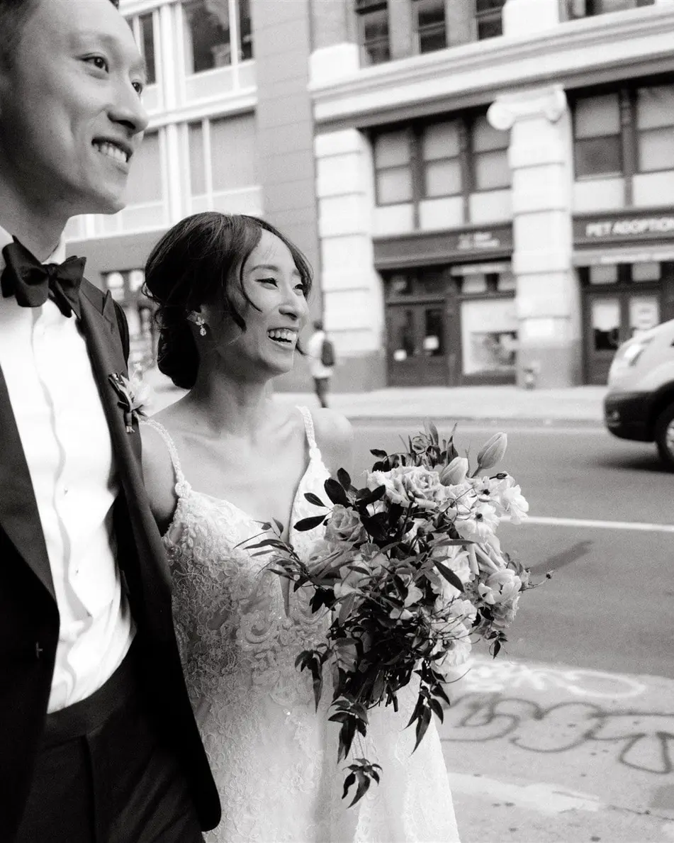 The groom laughs with the bride on a Tribeca sidewalk. Black and white.