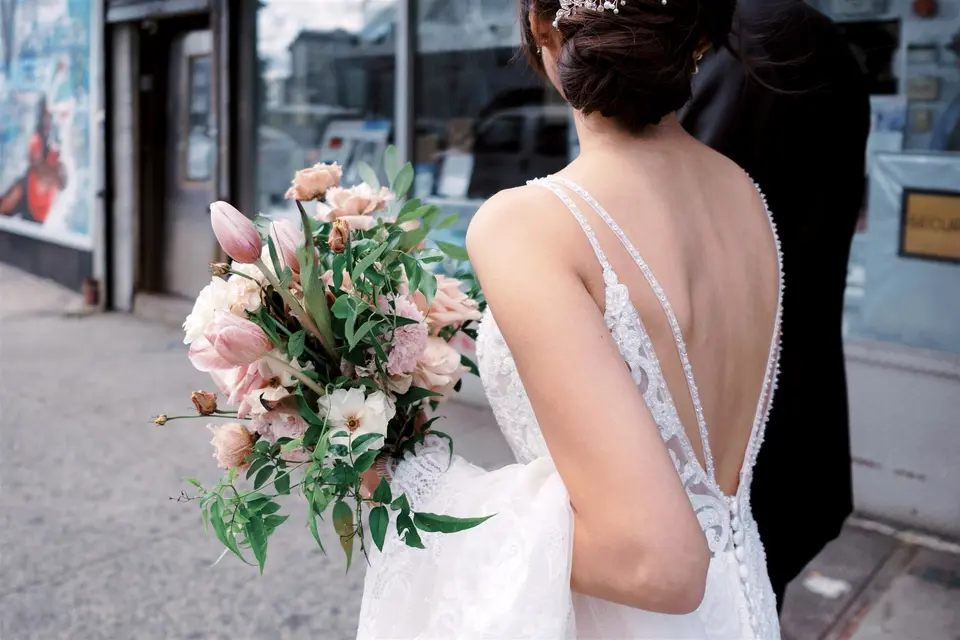 Seen from behind, the bride holds a loose bouquet of pink roses and tulips at her side.
