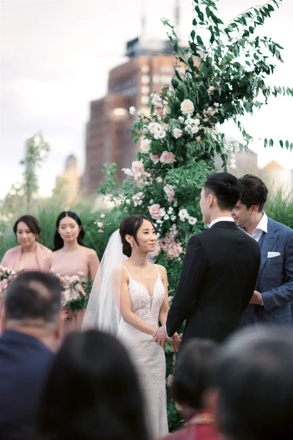The ceremony on the rooftop beneath an arch of pink flowers, the bridesmaids in blush beside the couple.