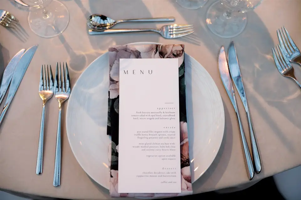 A menu card on a floral napkin at a place setting.