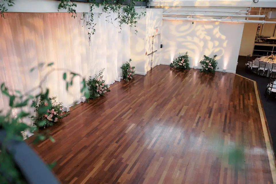The empty dance floor, draped walls lit with patterns of light and clusters of flowers along the edge.