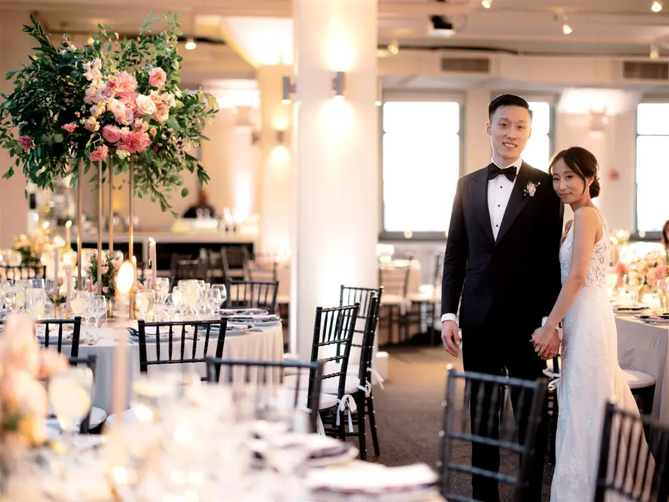 The bride and groom stand among the tables in the dining room.