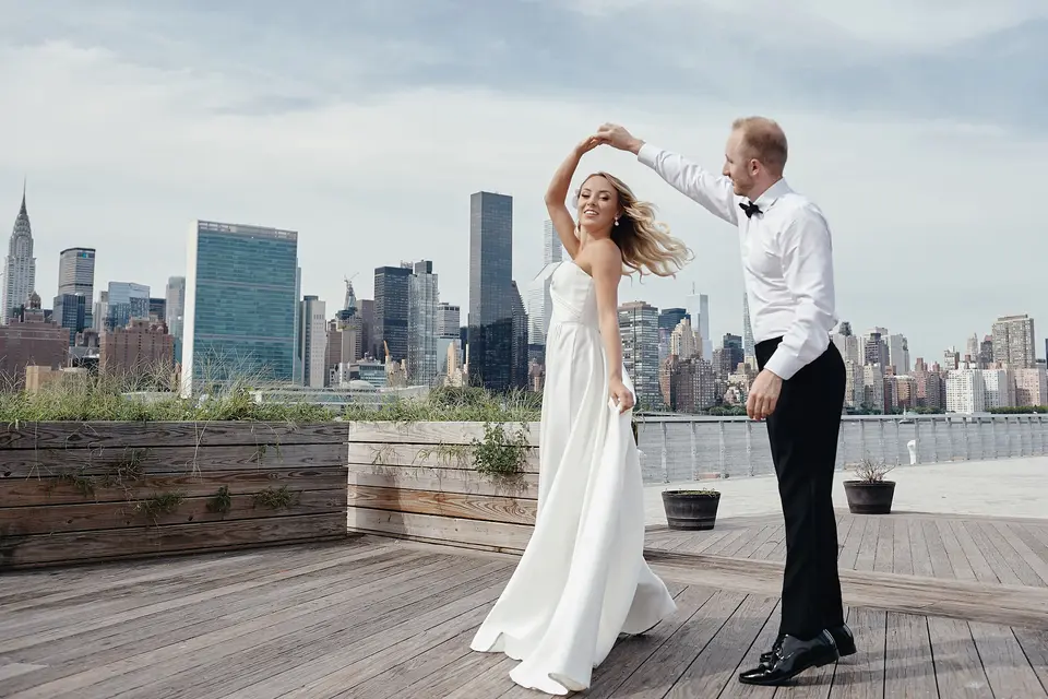 On a wooden deck by the East River, the groom twirls the bride, the Midtown skyline and the United Nations behind them.