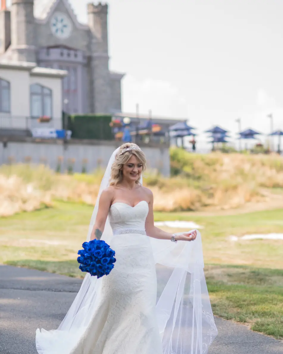 The bride walks across the lawn with a bouquet of blue roses, the stone castle behind her.