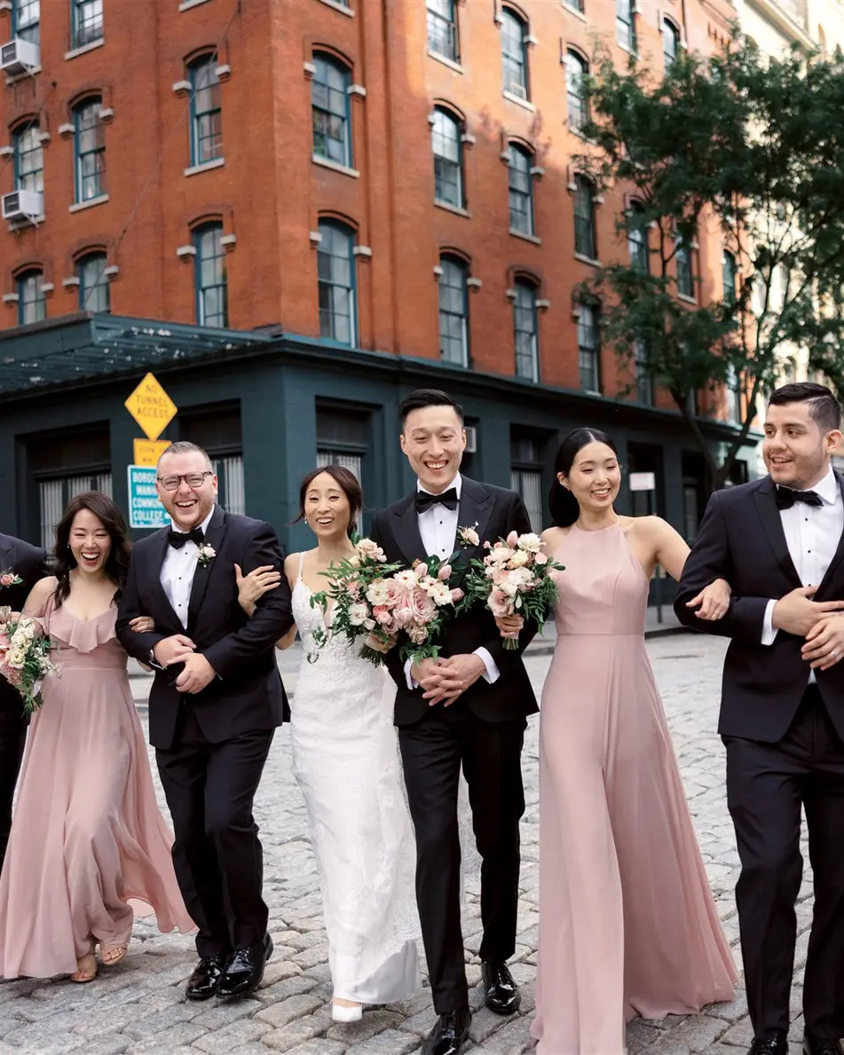 The wedding party walk arm in arm down a cobbled Tribeca street, bridesmaids in dusty pink and groomsmen in black tie.