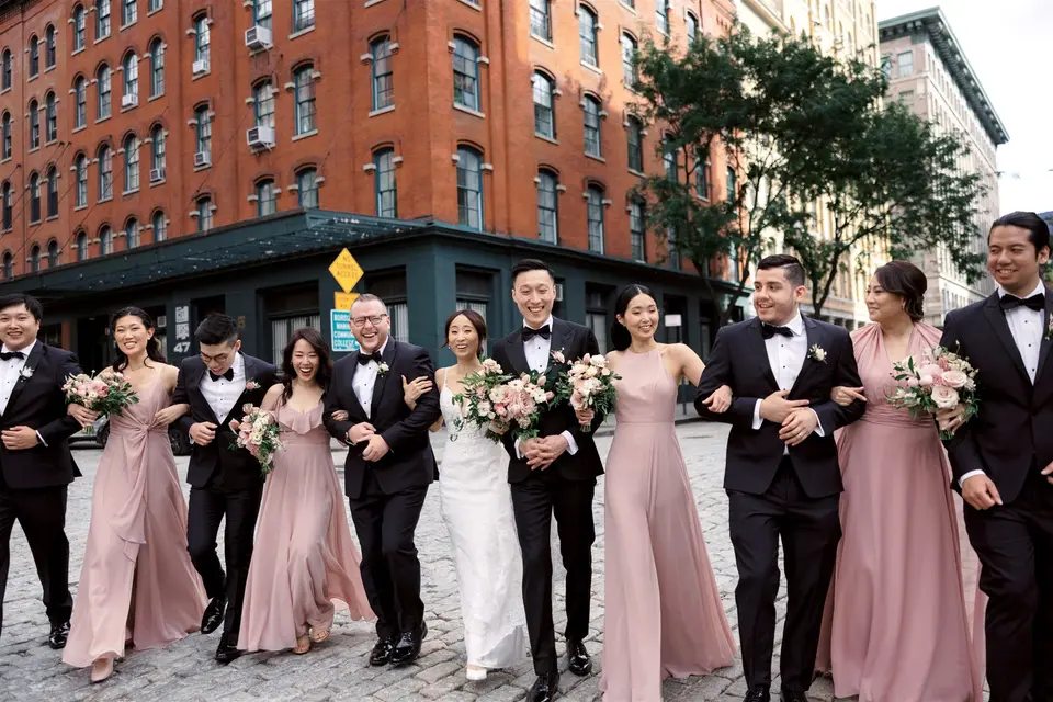 The wedding party walk arm in arm down a cobbled Tribeca street, bridesmaids in dusty pink and groomsmen in black tie.