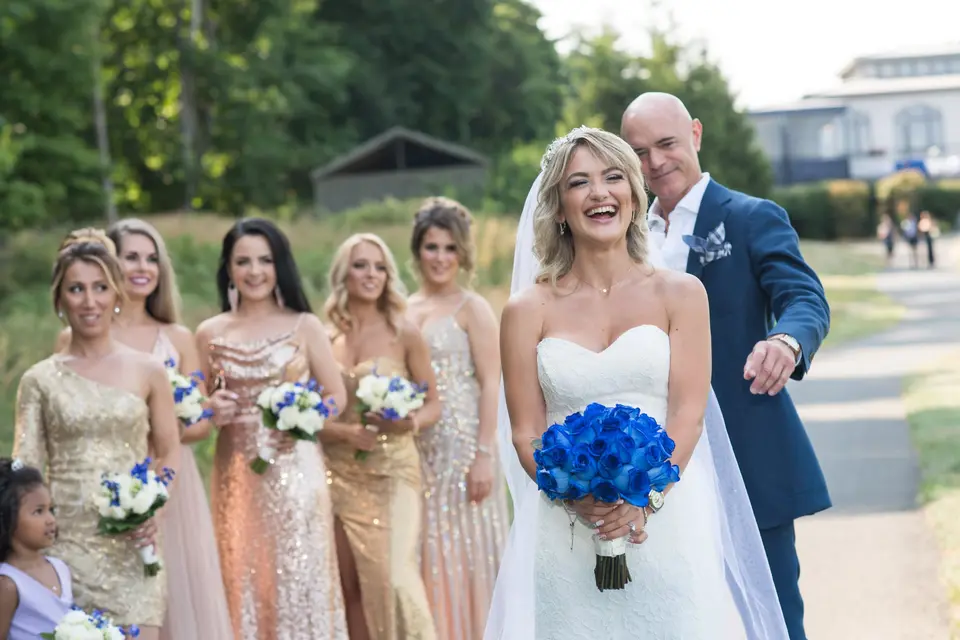 The groom taps the bride's shoulder and she laughs, the bridesmaids watching.