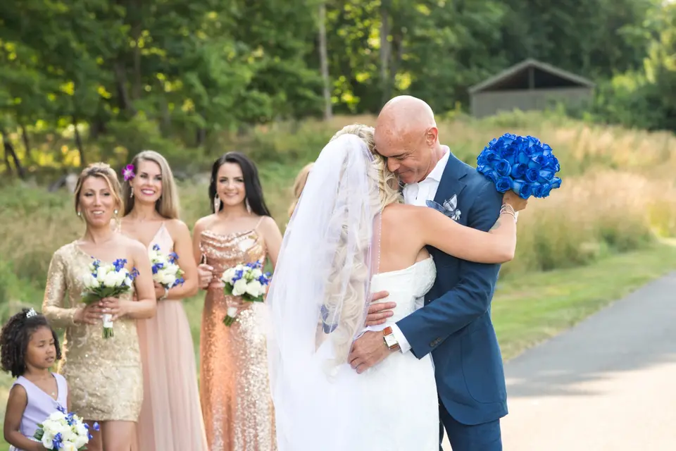 The bride and groom embrace at the first look, her bouquet of blue roses in his hand.