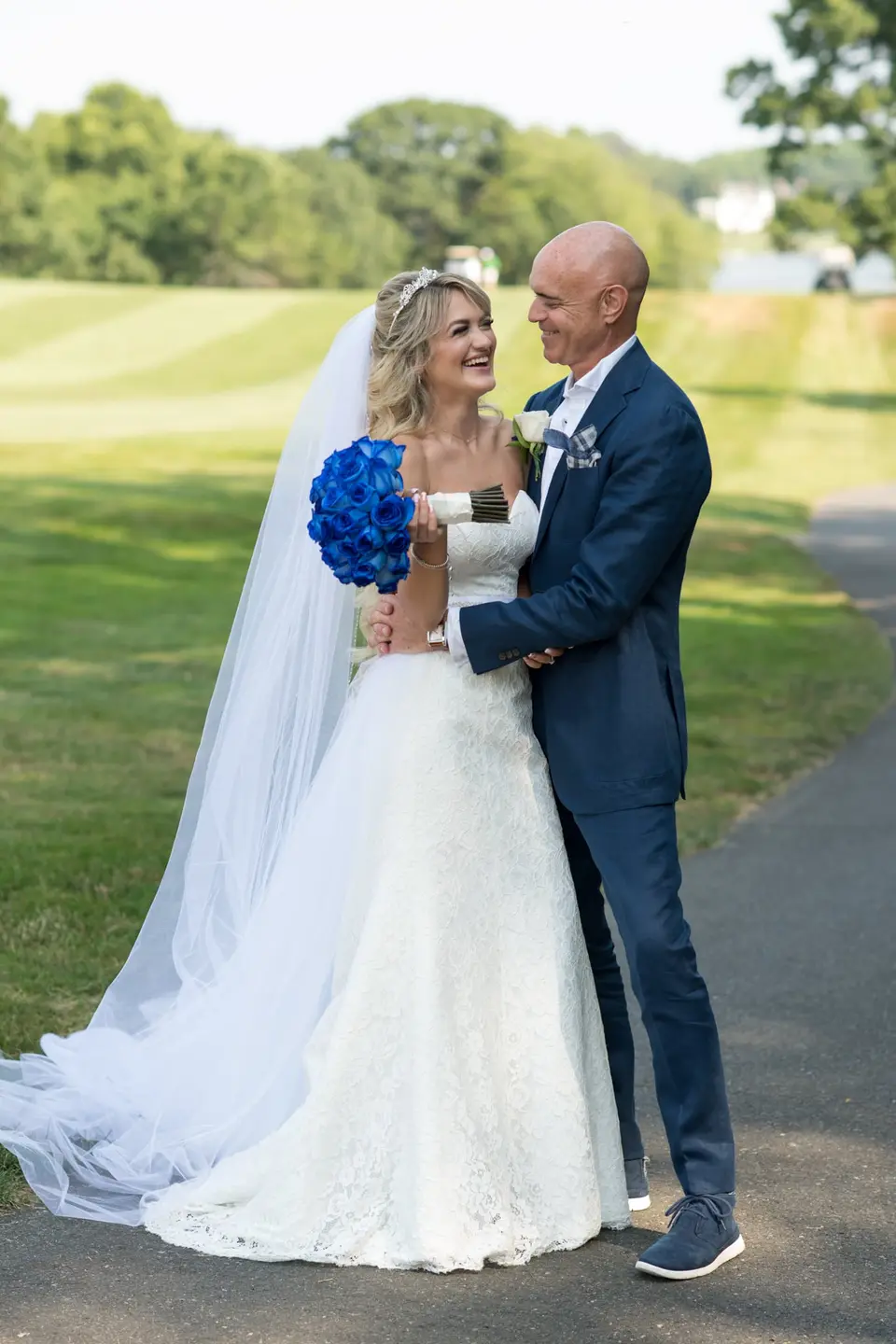 The groom holds the bride close on the lawn, both laughing.