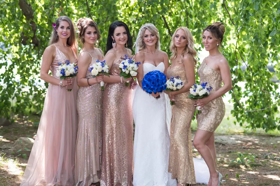 The bride among her bridesmaids in gold, blush and rose sequins beneath a willow.
